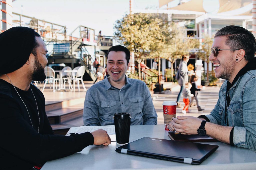 three young men drinking coffee outside